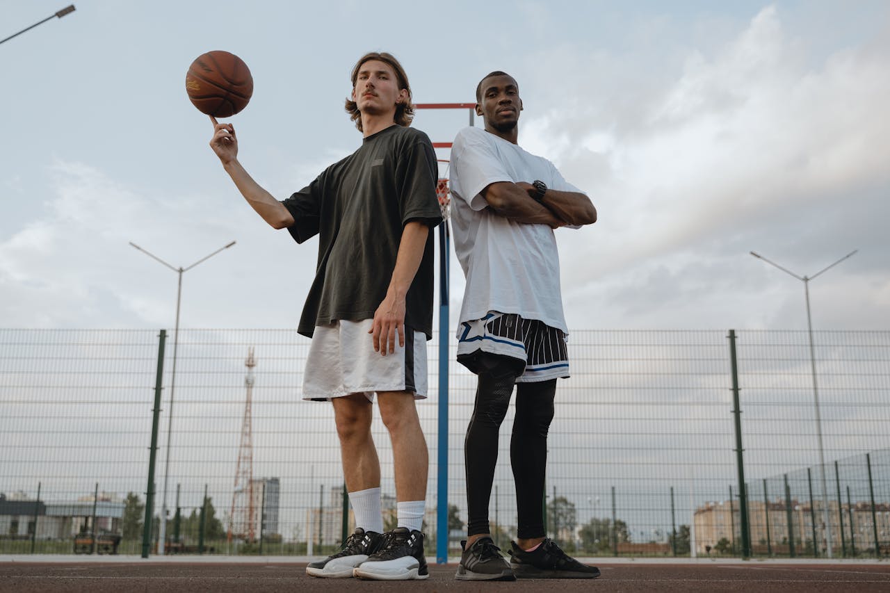 Two men posing with a basketball on an outdoor court, showcasing athletic skill.